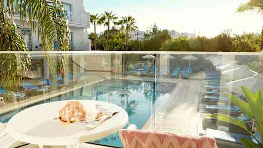 Utsikt fra en terrasse som viser et basseng med solsenger og parasoller omgitt av grøntområder. (AI-generert tekst)