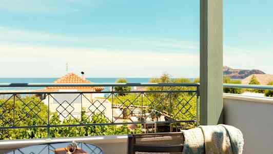 Utsikt fra en balkong med et glassbord og stol. Havet og hus kan sees i bakgrunnen. (AI-generert tekst)