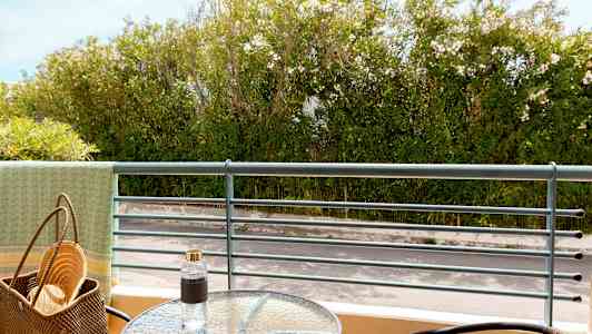 Utsikt fra en balkong med et glassbord, stoler og frodig vegetasjon i bakgrunnen. (AI-generert tekst)