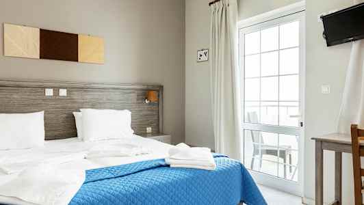 Et hotellrom med en dobbeltseng, blått sengeteppe og hvitt sengetøy. (AI-generert tekst)