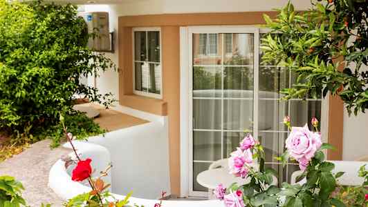 Inngang med hvit fasade og en terrasse dekorert med roser og vegetasjon. (AI-generert tekst)