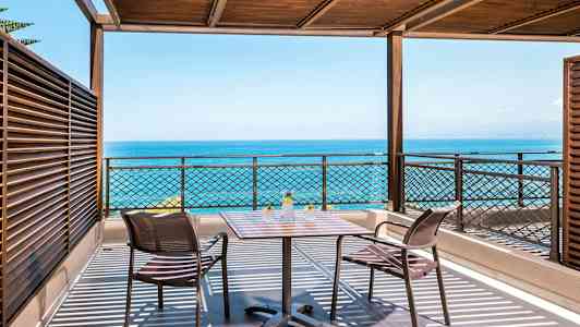 Terrasse med havutsikt, bord og to stoler under trepergola. (AI-generert tekst)