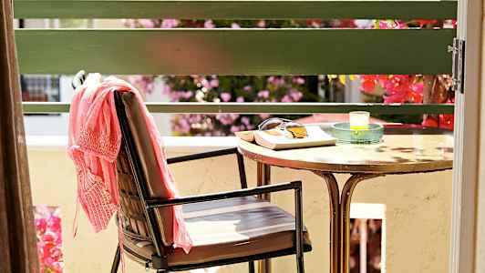 En stol med et rosa klesplagg, et bord med solbriller, en bok og et lys står på en terrasse. (AI-generert tekst)