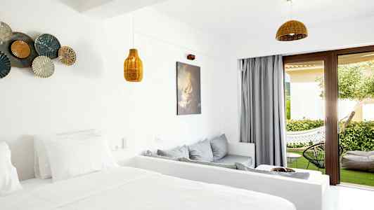 Et hotellrom med lys innredning og åpning mot en terrasse med grønne omgivelser. (AI-generert tekst)