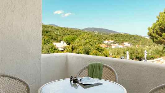 Utsikt fra en balkong med et bord, solbriller og avis, samt grønne omgivelser. (AI-generert tekst)