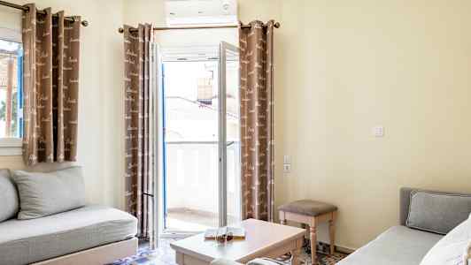 Bilde av en lys stue med to sofaer, et sofabord og gardiner foran en balkongdør. (AI-generert tekst)