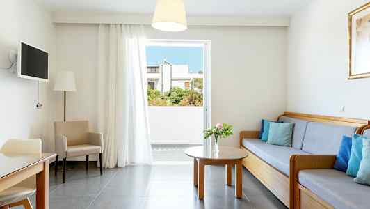 Et lyst oppholdsrom med en sofa, bord og stoler, samt en åpning mot balkongen. (AI-generert tekst)