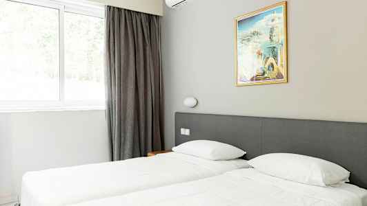 Et rom med to enkeltsenger, et maleri og et vindu med gardiner. (AI-generert tekst)