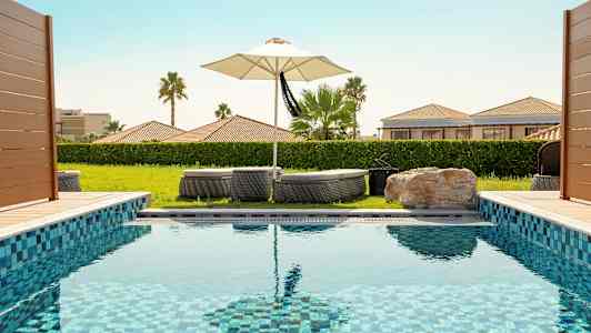 Et svømmebasseng med solsenger og en parasoll i bakgrunnen. (AI-generert tekst)