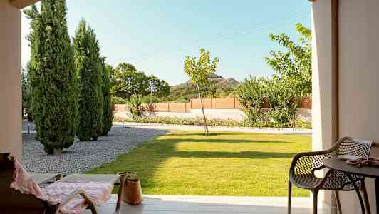 Utsikt fra en terrasse med stoler og bord, plen og trær i bakgrunnen. (AI-generert tekst)