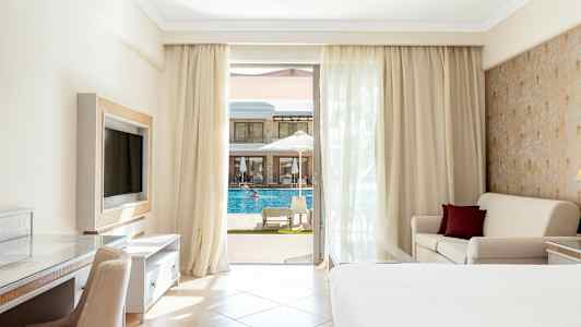 Hotellrom med balkong, seng, sofa og utsikt mot et basseng. (AI-generert tekst)