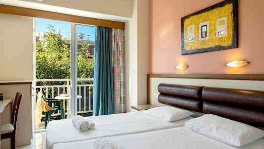 Et hotellrom med dobbeltseng, sengelamper, skrivebord og en balkong med utsikt over grøntområder. (AI-generert tekst)