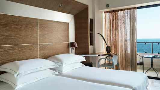 Hotellrom med to enkeltsenger, skrivebord og havutsikt. (AI-generert tekst)