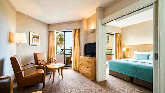 Et hotellrom med sittegruppe, TV og seng med blått sengeteppe. (AI-generert tekst)