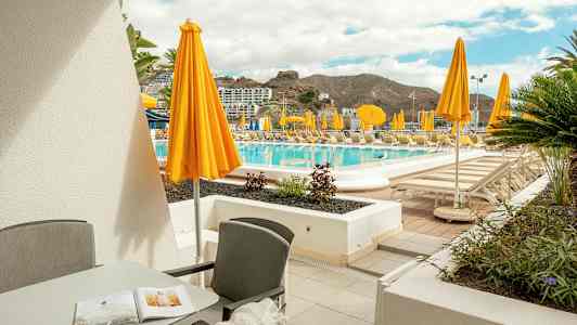 Terrasse med møbler og utsikt over bassengområde med gule parasoller. (AI-generert tekst)