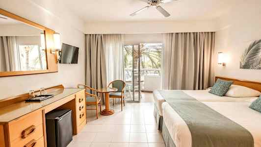 Hotellrom med to senger, et skrivebord, en flatskjerm-TV og en balkong med utsikt. (AI-generert tekst)