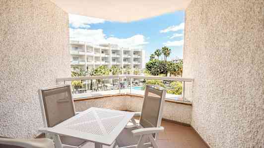 En balkong med utemøbler, utsikt mot et hotell med palmer og basseng. (AI-generert tekst)