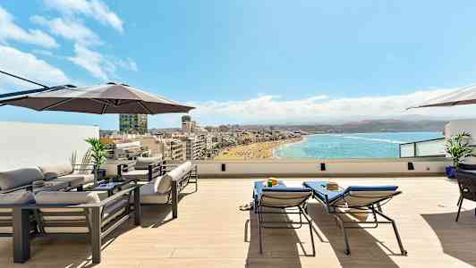Takterrasse med møbler, parasoll og utsikt over en strand og havet. (AI-generert tekst)