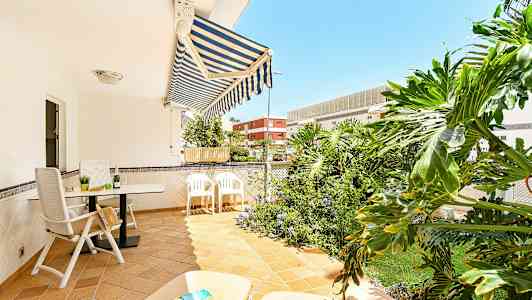 En terrasse med utemøbler, markise og grønne planter i bakgrunnen. (AI-generert tekst)