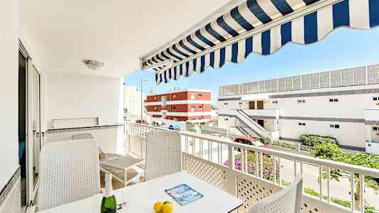 En balkong med møbler, parasoll og utsikt mot bygninger. (AI-generert tekst)