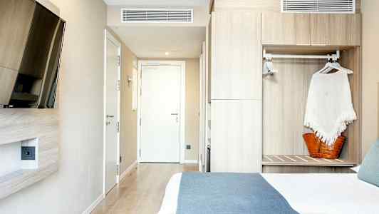 Et hotellrom med en seng, en veggmontert TV og et skap. (AI-generert tekst)