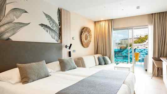 Et moderne hotellrom med to senger, lys innredning og en balkong med utsikt mot et basseng og bygninger. (AI-generert tekst)