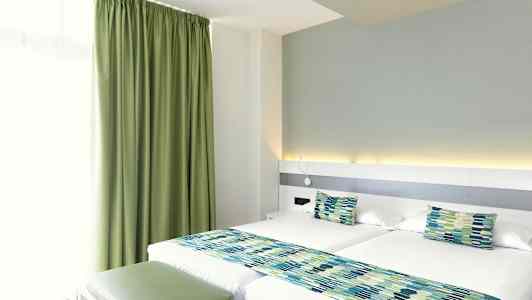 Et hotellrom med to enkeltsenger, grønne gardiner og matchende sengedekorasjoner. (AI-generert tekst)