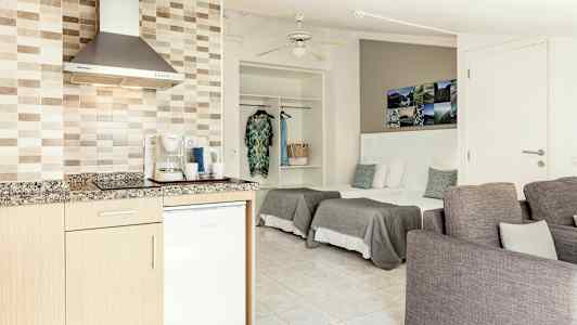 Et åpent hotellrom med en kjøkkenkrok, senger og sittemøbler. (AI-generert tekst)