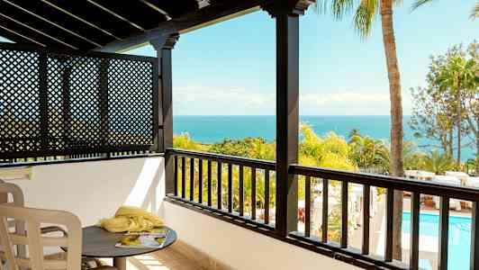 Utsikt fra en balkong med hav, palmer og basseng i bakgrunnen. (AI-generert tekst)