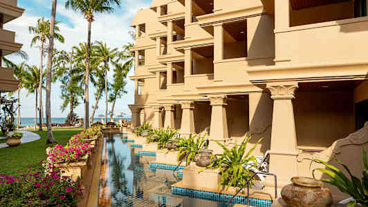 Bygning med flere balkonger, omgitt av plener, palmer og et basseng. (AI-generert tekst)