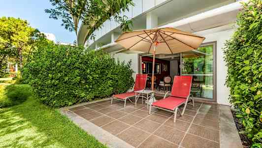 En uteplass med to røde solsenger, en parasoll og grønne omgivelser. (AI-generert tekst)