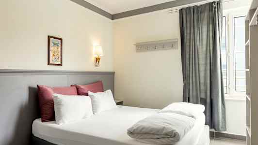 Bilde av et hotellrom med en dobbeltseng, dekorert med sengetøy i hvitt og rødt samt en lys grå sengegavl. (AI-generert tekst)