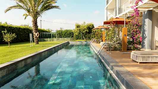 En lang smal basseng omgitt av grøntområder og en moderne bolig. (AI-generert tekst)