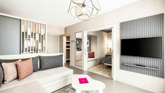 Et romslig og moderne innredet hotellrom med sittegruppe, soveplass og en veggmontert TV. (AI-generert tekst)