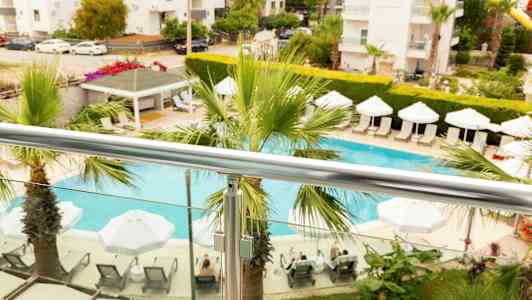 Utsikt fra balkongen med et basseng, parasoller og solsenger omgitt av planter. (AI-generert tekst)