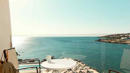 En balkong med utsikt over havet, parasoller ved et basseng og en kopp på et bord. (AI-generert tekst)