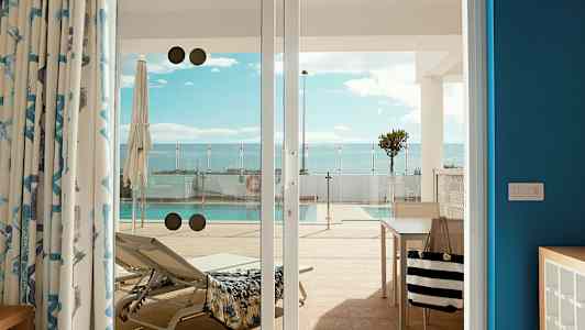 Bilde av en solseng og et basseng, sett fra en terrasse gjennom glassdører. (AI-generert tekst)