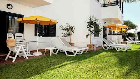 Grønt område med solsenger og parasoller ved en hvit bygning. (AI-generert tekst)