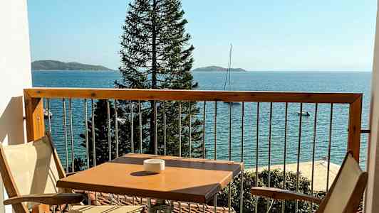 En balkong med to stoler og et bord, havet og en mast vises i bakgrunnen. (AI-generert tekst)