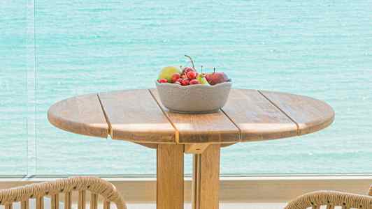 Et trebord med stoler, en bolle med frukt og utsikt over havet. (AI-generert tekst)