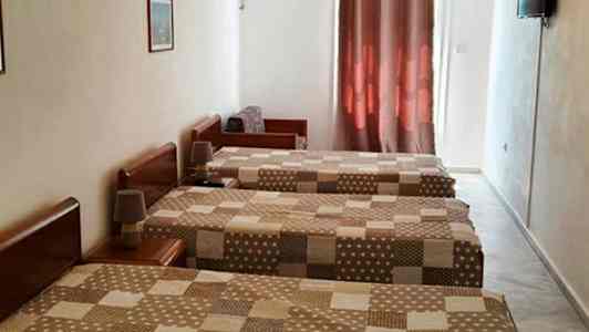 Tre enkeltsenger på et hotellrom med brunmønstrede dynetrekk, klimaanlegg og en TV på veggen. (AI-generert tekst)