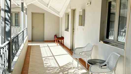 En åpen balkong med hvite møbler, et bord og en klimaanlegg på veggen. (AI-generert tekst)