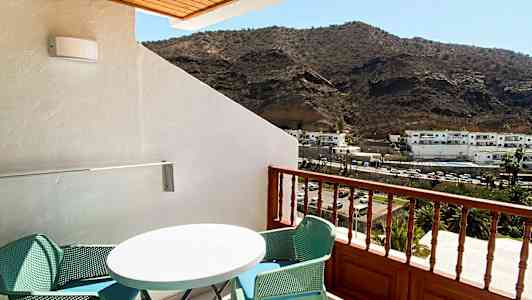 En balkong med møbler og utsikt mot fjell. (AI-generert tekst)