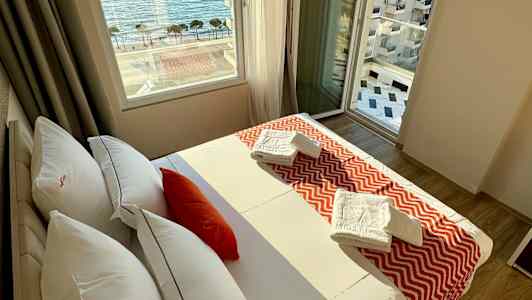 Et hotellrom med en seng, vindu med havutsikt og håndklær på sengen. (AI-generert tekst)