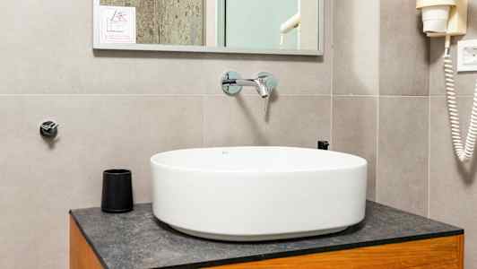 Et baderom med en rund servantbolle på et treskap, et speil over og detaljer som en dusj og hårføner synlig. (AI-generert tekst)