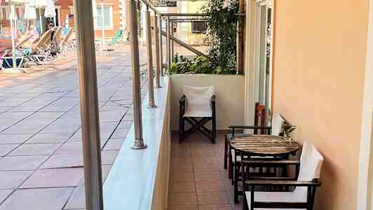 En uteplass med bord og stoler ved en gangvei nær et bassengområde. (AI-generert tekst)