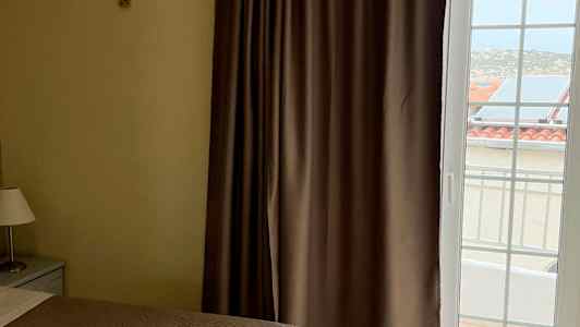 To senger med brune sengetepper, et vindu med gardiner og utsikt mot bygninger utenfor. (AI-generert tekst)