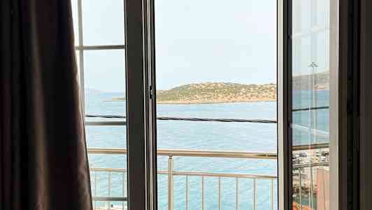 Utsikt fra et åpent vindu med en balkong, havet og en øy i bakgrunnen. (AI-generert tekst)