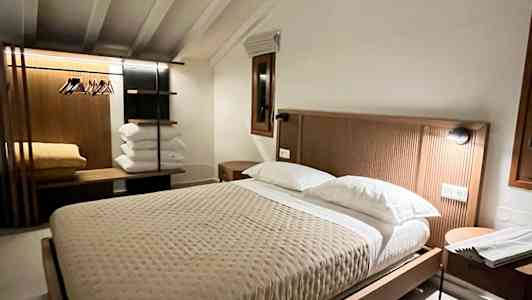 Et varmt innredet soverom med en stor seng, nattbord og et klesstativ. (AI-generert tekst)