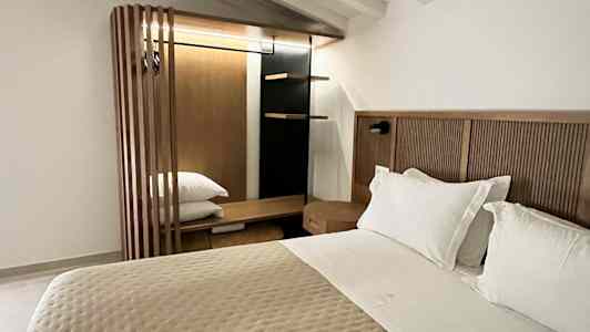 Et soverom med en dobbeltseng, hvit takpanel og en garderobe i tre. (AI-generert tekst)